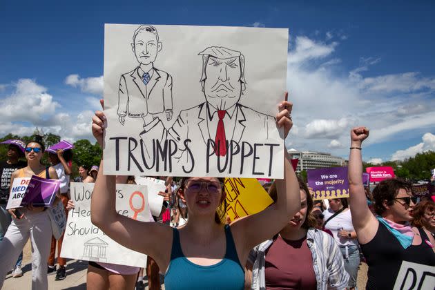 An abortion rights activist holds a sign with a sketch of Judge Matthew Kacsmaryk and former President Donald Trump, with 