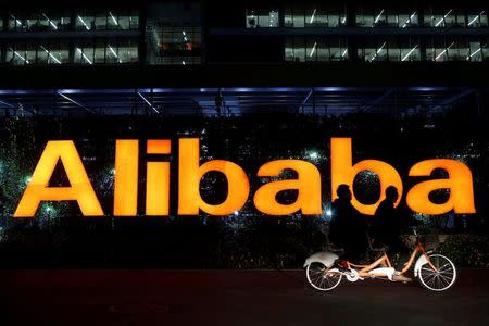 FILE PHOTO: People ride a double bicycle past a logo of The Alibaba Group at the company's headquarters on the outskirts of Hangzhou, Zhejiang province November 10, 2014. REUTERS/Aly Song/File Photo