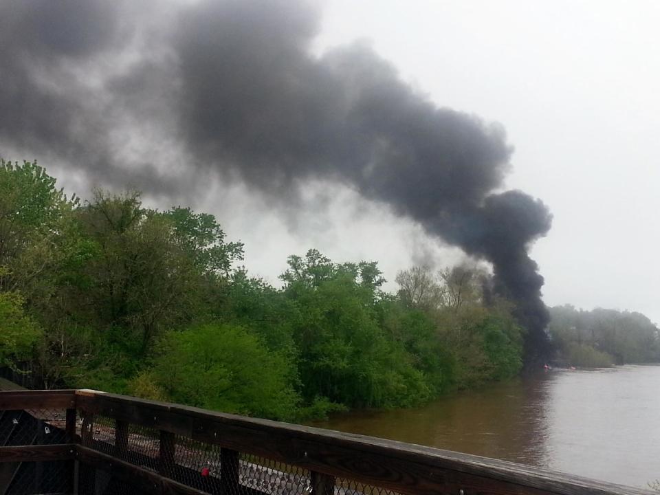 This mobile phone photo provided Ali Hallock shows smoke rising after several CSX tanker cars carrying crude oil derailed, from the view of a bridge over the James river, Wednesday, April 30, 2014, in Lynchburg, Va. Authorities evacuated numerous buildings Wednesday after the derailment. (AP Photo/Ali Hallock) MANDATORY CREDIT