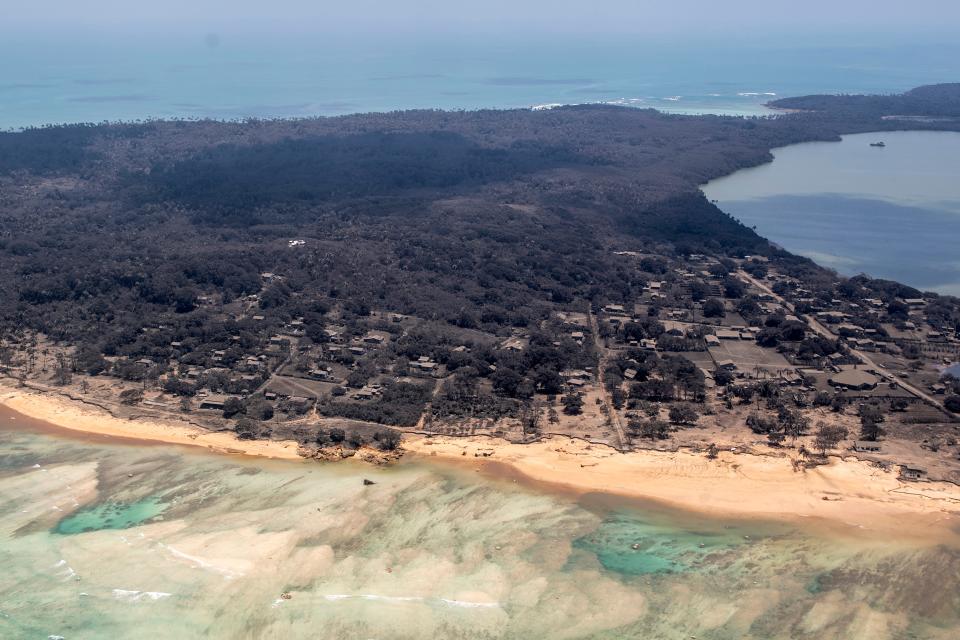 In this photo provided by the New Zealand Defense Force, volcanic ash covers roof tops and vegetation in an area of Tonga, Monday, Jan. 17, 2022. Thick ash on an airport runway was delaying aid deliveries to the Pacific island nation of Tonga, where significant damage was being reported days after a huge undersea volcanic eruption and tsunami.