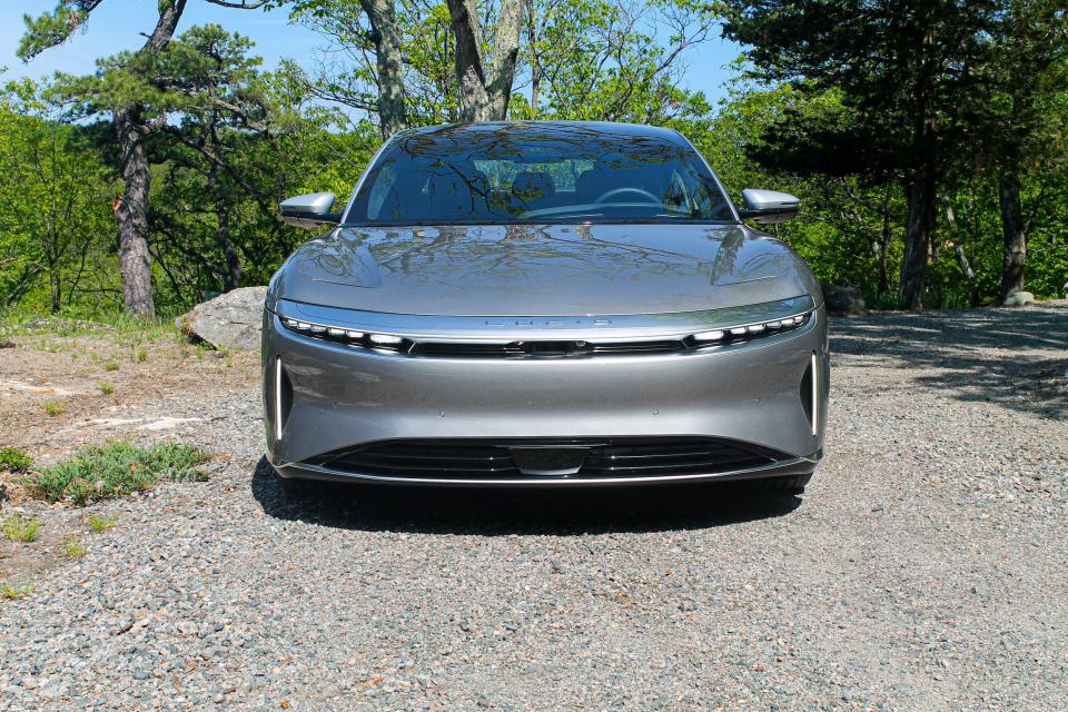 A silver Lucid Air Grand Touring Performance electric car in a driveway, with trees and blue sky in the background.