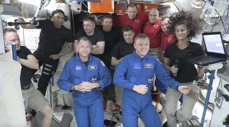 En esta imagen tomada de una transmisión en vivo de la NASA, los dos astronautas atrapados en la Estación Espacial Internacional desde junio de 2024, Butch Wilmore, a la izquierda, y Suni Williams, a la derecha, dan la bienvenida a dos nuevos residentes que volaron en SpaceX, Nick Hague de la NASA, al frente a la izquierda en azul, y Alexander Gorbunov de la Agencia Espacial Rusa, al frente a la derecha en azul