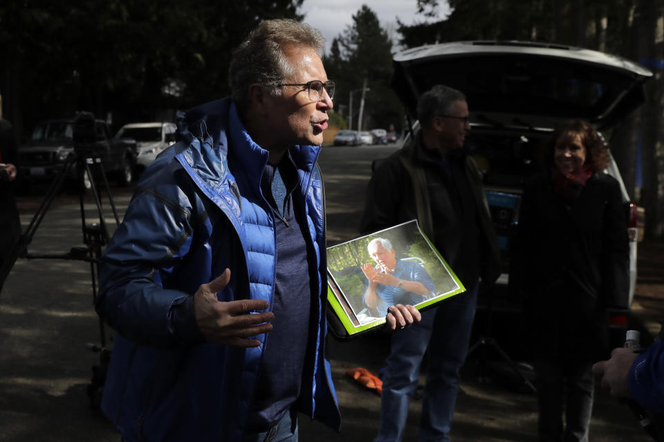 In this March 12, 2020 photo, Scott Sedlacek becomes animated as he holds a picture of his father, Chuck, and talks to reporters outside Life Care Center in Kirkland, Wash., near Seattle. The facility has been at the center of the COVID-19 coronavirus outbreak in the state, and Sedlacek — who also has tested positive for the virus — said he and his siblings have barely spoken to their father who lives inside the center, and in addition to testing positive for the coronavirus, has blindness, neuropathy, and has difficulty using a phone, saying he is more of an "inmate" than a patient. Residents of assisted living facilities and their loved ones are facing a grim situation as the coronavirus spreads across the country, placing elderly people especially at risk. (AP Photo/Ted S. Warren)