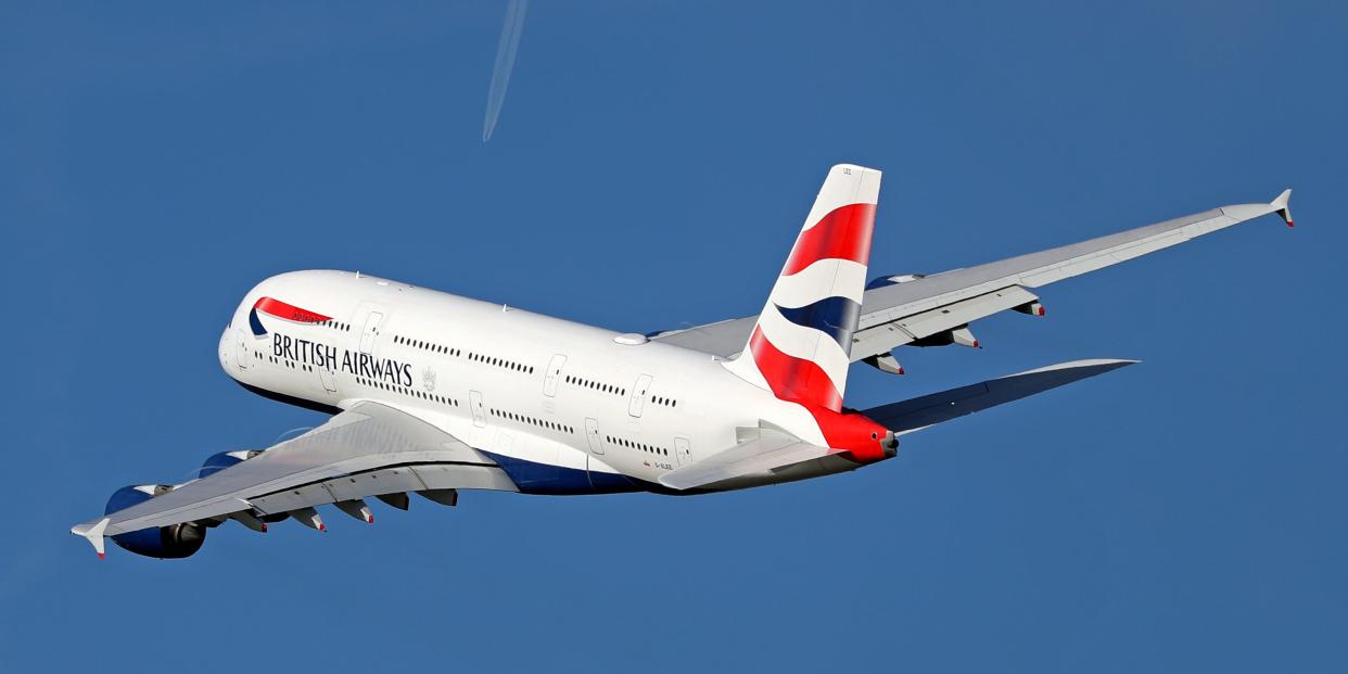 A British Airways Airbus A380 flies across a blue sky with the trail of a smaller plane visible in the far distance