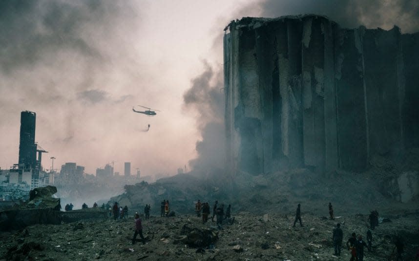 An army helicopter drops water at the smouldering scene of the explosion - EYEVINE