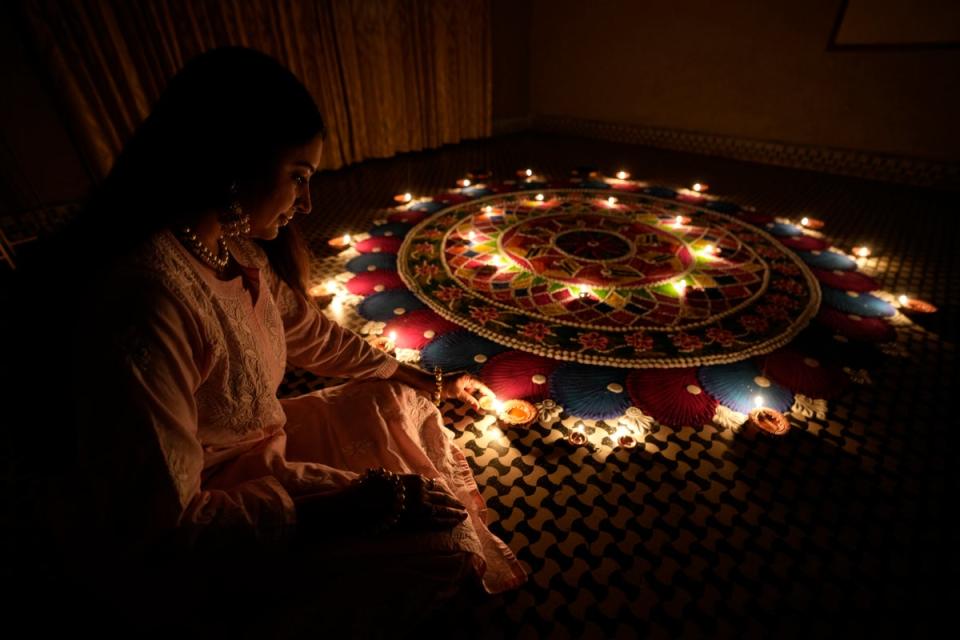 A girl lights an earthen lamp beside a rangoli, a hand decorated pattern on the floor, as part of Diwali festivities in Ahmedabad on 9 November (AP)