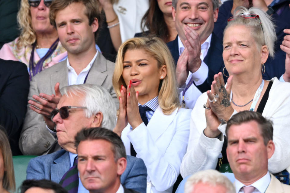 Zendaya in the stands clapping at an event, surrounded by a group of spectators