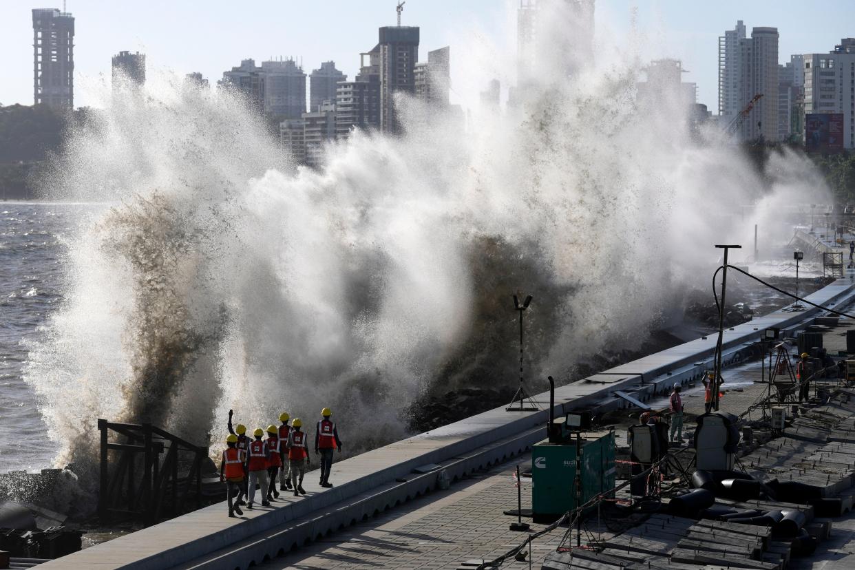 Coastal road workers walk as waves hit the city's waterfront during high tide in the Arabian Sea at Marine Drive in Mumbai (AP)