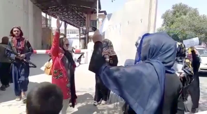 Women chant slogans as they protest next to an armed man, in Kabul