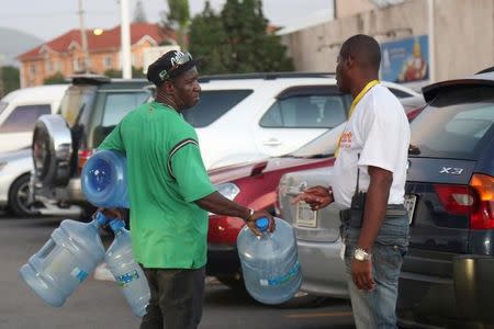 A man carries empty water containers while chatting with another man outside a supermarket, pending the arrival of Hurricane Matthew in Kingston, Jamaica, September 30, 2016. REUTERS/Gilbert Bellamy