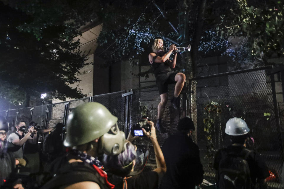 A demonstrator plays a trumpet from atop a steel fence during a Black Lives Matter protest at the Mark O. Hatfield United States Courthouse Sunday, July 26, 2020, in Portland, Ore. (AP Photo/Marcio Jose Sanchez)