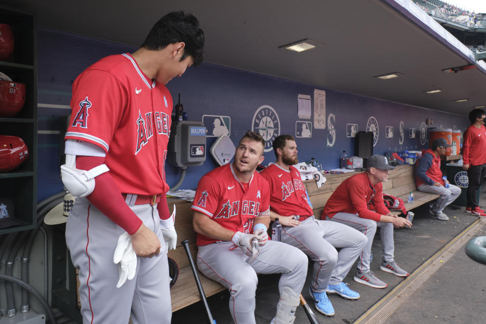 Los Angeles Angels' Shohei Ohtani, left, talks with Mike Trout, left on the bench, as they prepare to bat against the Seattle Mariners during the fourth inning of a baseball game, Sunday, June 19, 2022, in Seattle. (AP Photo/John Froschauer)