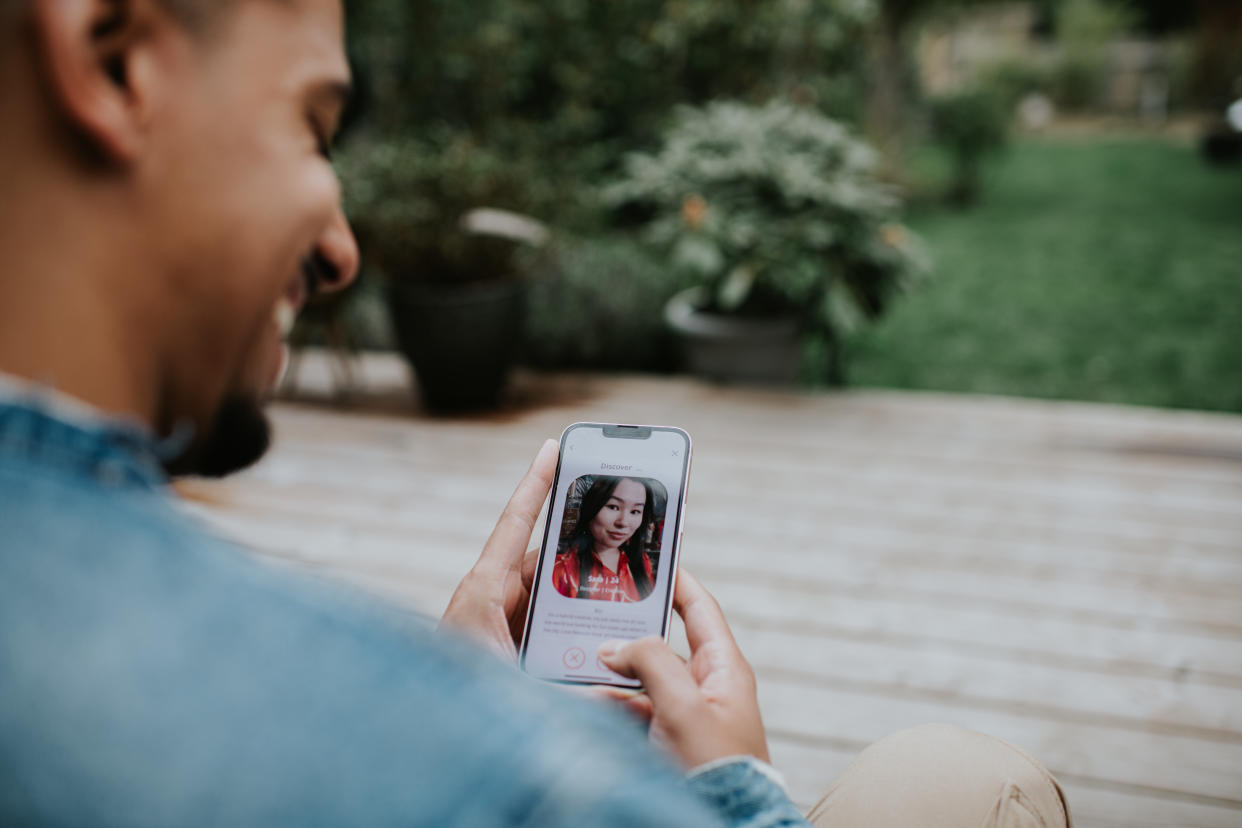 Close-up of a male holding a smart phone, and browsing a dating application. He looks at a photo of a woman and smiles.