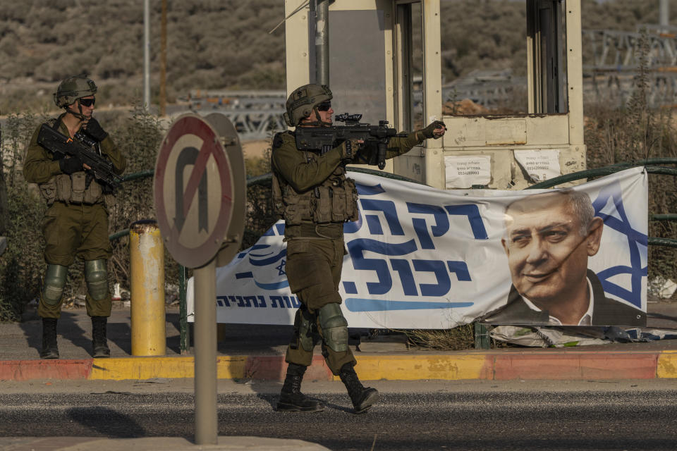 FILE - Israeli soldiers gesture to a vehicle at Tapuah Junction, next to a campaign poster for former Israeli Prime Minister Benjamin Netanyahu near the West Bank town of Nablus, Sunday, Oct. 16, 2022. News of the apparent comeback of former Prime Minister Benjamin Netanyahu and the dramatic rise of his far-right and ultra-Orthodox allies has elicited little more than a shrug among many Palestinians. (AP Photo/Tsafrir Abayov, File)