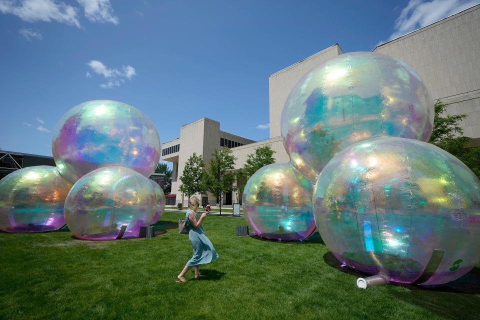 A woman takes a photo of the Evanescent bubble exhibit outside the Marcus Performing Arts Center in  Milwaukee on Monday, July 17, 2023. The exhibit consists of three sets of four bubbles each made from a color-reflecting material that reacts to the changing light of the sun as it moves across the sky.