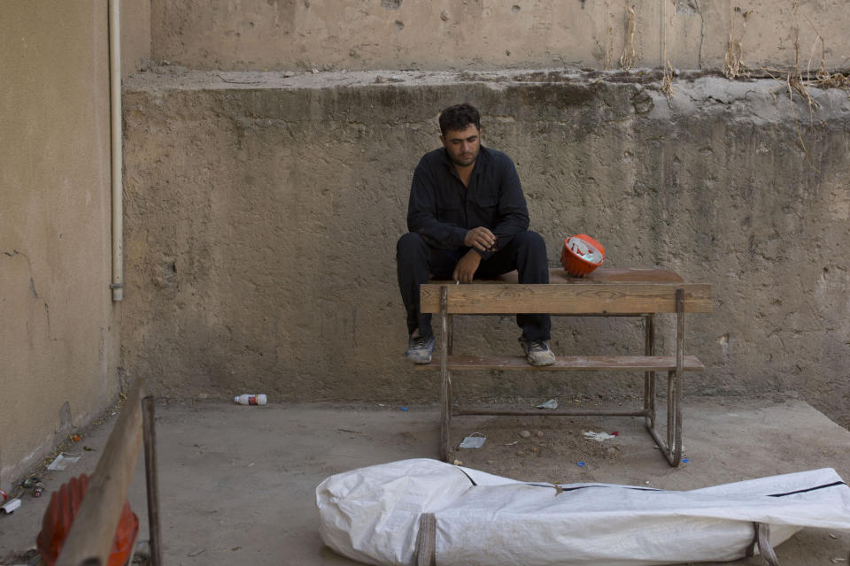 FILE - In this Saturday, Sept. 7, 2019, file, photo, a first responder smokes after removing a body at the site of a mass grave in Raqqa, Syria. The recently exhumed makeshift mass grave is the 16th found in Raqqa and its surrounding countryside since Islamic State militants were driven out of the area in 2017. (AP Photo/Maya Alleruzzo, File)