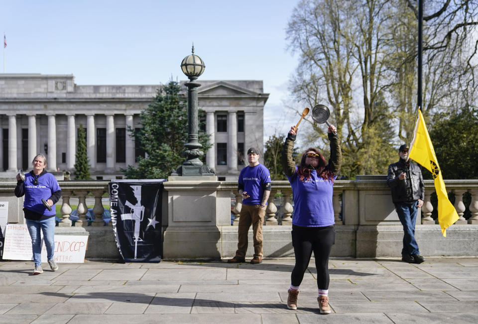 Ryan Olski, second from right, bangs on a pot as the group "We the People Against Communism" protest before the signing of firearms regulation bills by Washington Gov. Jay Inslee, Tuesday, April 25, 2023, outside the Capitol in Olympia, Wash. (AP Photo/Lindsey Wasson)