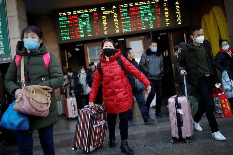 People wearing face masks carry their luggage as they walk outside Beijing Railway Station as the country is hit by an outbreak of the new coronavirus, in Beijing