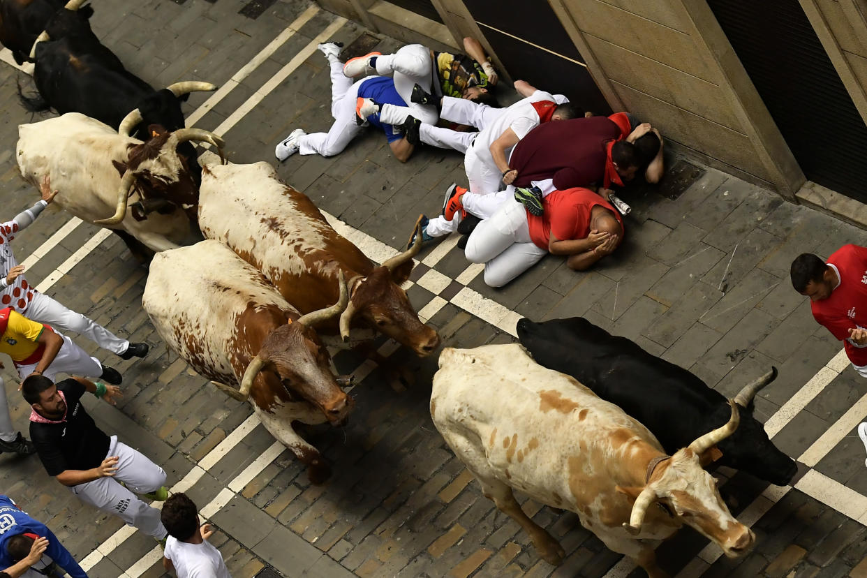 Revelers who have fallen on the ground try to protect themselves by covering their heads with their hands as the animals run by on the third day of the running of the bulls.