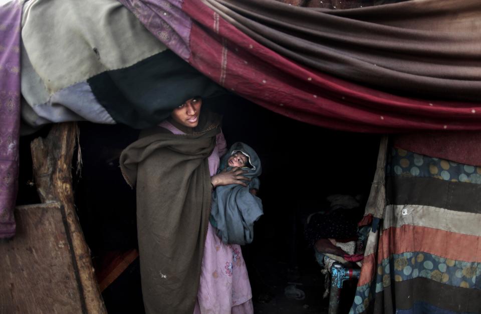 In this Sunday, Jan. 6, 2013 photo, a Pakistani woman who claims that her daughter has a fever, stands at the doorway of her makeshift tent waiting for her brother's arrival to take her daughter to a clinic to be examined, in Rawalpindi, Pakistan. Wonder Woman and Supergirl now have a Pakistani counterpart in the pantheon of female superheroes _ one who shows a lot less skin. Meet Burka Avenger: a mild-mannered teacher with secret martial arts skills who uses a flowing black burka to hide her identity as she fights local thugs seeking to shut down the girls' school where she works. Sadly, it's a battle Pakistanis are all too familiar with in the real world.(AP Photo/Muhammed Muheisen)