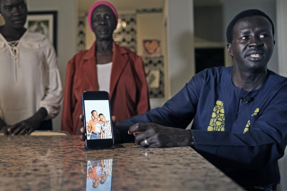 Jacob Mabil, right, speaks while showing a cell phone photo of hie nieces Nyanluak Deng, left, and Anyier Deng during an interview at his home Wednesday, Nov. 8, 2023, in Haslet, Texas. Looking on are the girl's grandmother Adeng Ajang and Mabil's wife Akuot Leek. (AP Photo/LM Otero)