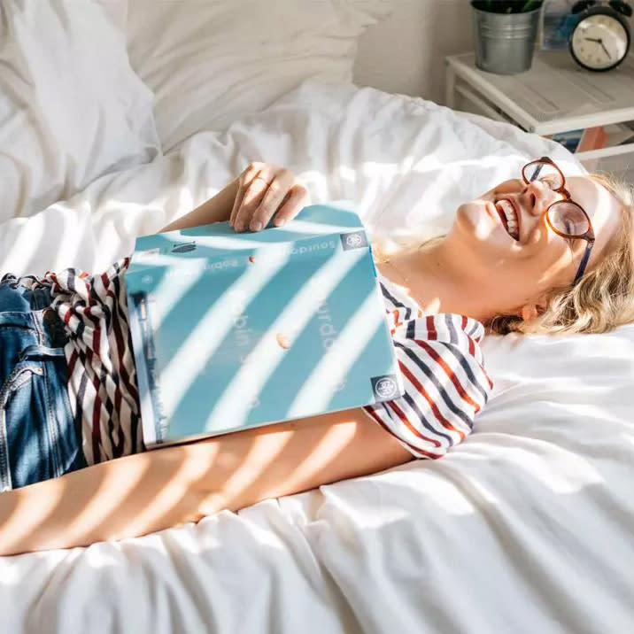 woman with a book laying on her body smiling in bed