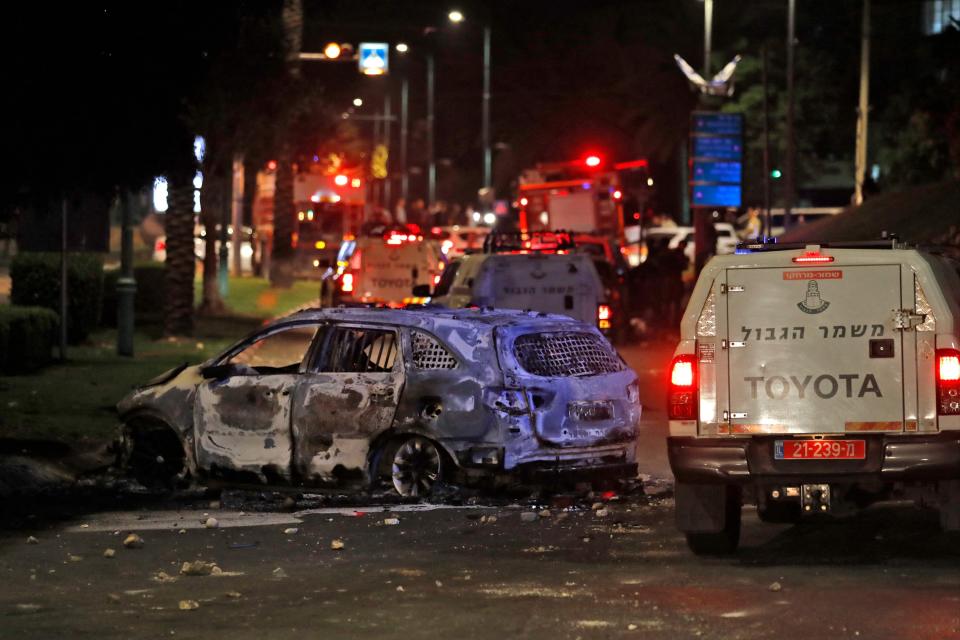 Israeli border police vehicles drive past an extinguished burnt vehicle in Lod near Tel Aviv (AFP via Getty Images)