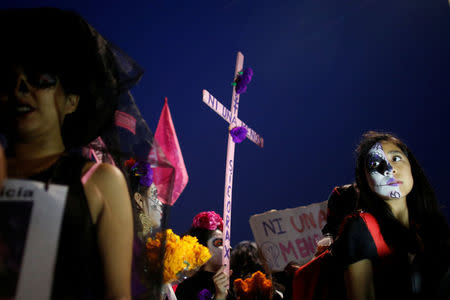 An activist with her face painted to look like the popular Mexican figure "Catrina" holds a cross as she takes part in a march against femicide during the Day of the Dead in Mexico City, Mexico, November 1, 2017. The words on the cross read: "No one more". REUTERS/Carlos Jasso