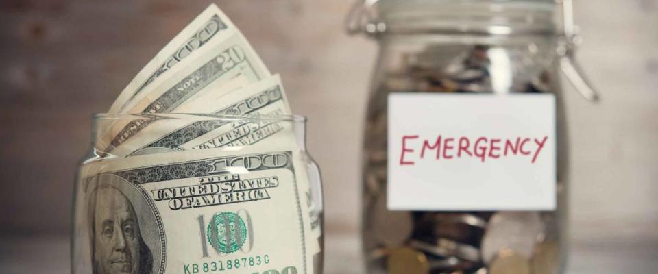 Dollars and coins in glass jar with emergency label.