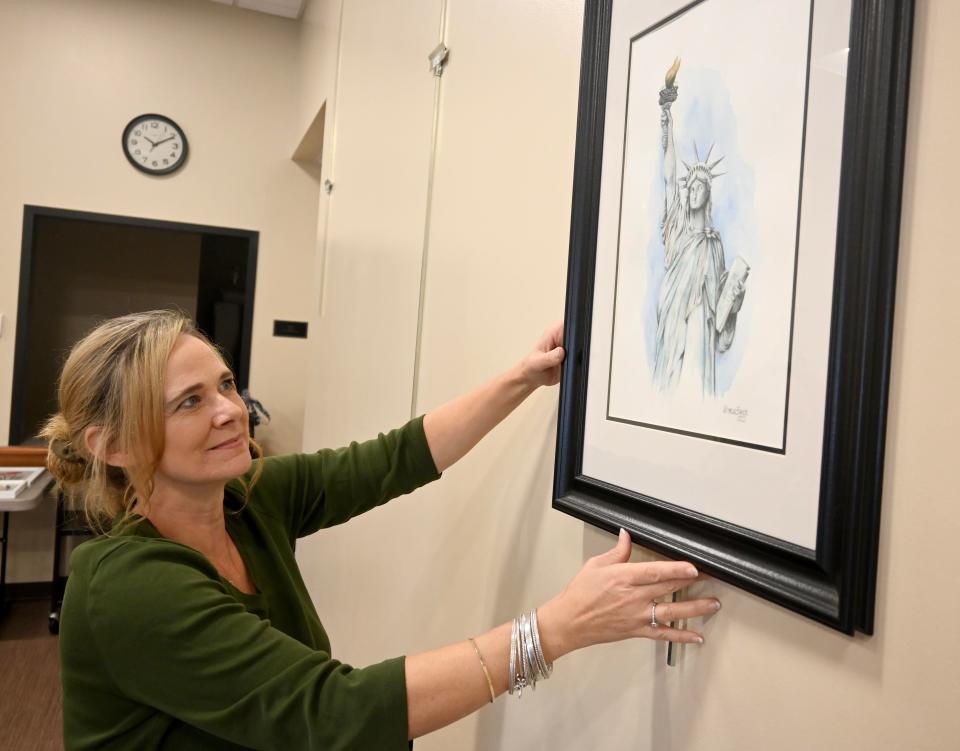 Hampstead artist Michelle Baker hangs artwork to be auctioned off to benefit veterans in need of assistance with heating bills this winter at the Kingston Community Library.