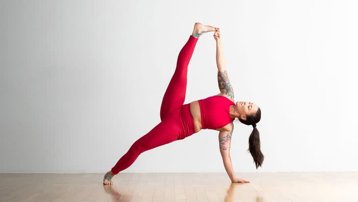 A person demonstrates a variation of Side Plank in yoga, grabbing the toes of the top foot