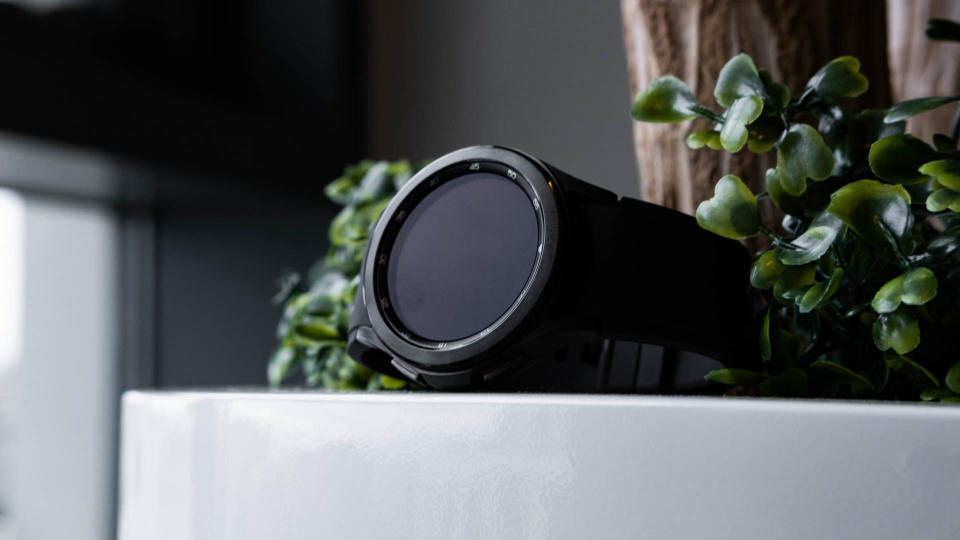 A black Samsung Galaxy Watch 4 Classic nestled in some foliage on a planter.