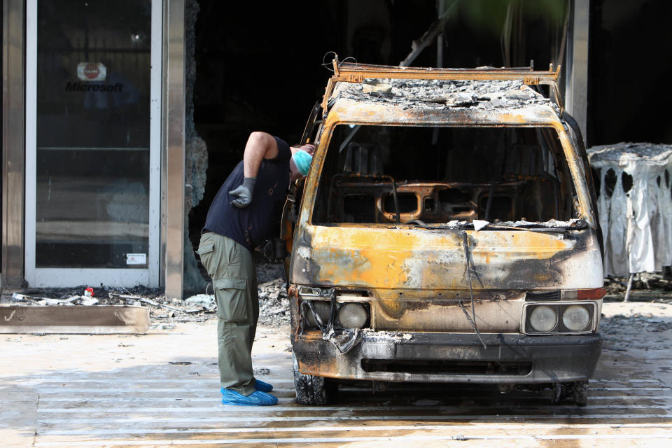 A police officer investigates a destroyed van outside the entrance of Microsoft office in northern Athens, Wednesday, June 27, 2012. Assailants attacked the offices of Microsoft in Athens early Wednesday, driving a van through the front doors and setting off an incendiary device that burned the building entrance, police said. There were no reports of injuries in the pre-dawn attack on the U.S. company's headquarters in the Greek capital, located in the Maroussi suburb north of the city center. (AP Photo/Thanassis Stavrakis)