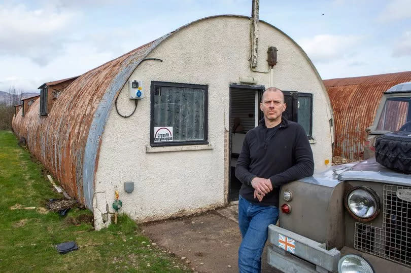 Miles Kay stands outside hut 55, which now homes his own CrossFit business, while leaning on his car