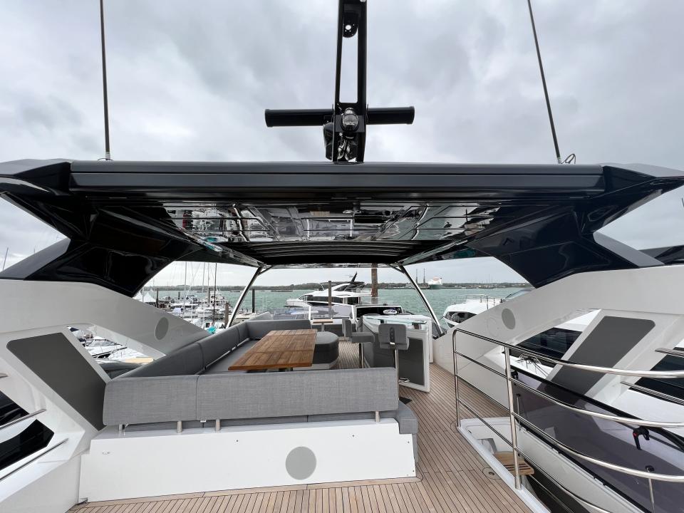 The flybridge of. Sunseeker 76 features a large u-shaped grey couch and a small bar with two stools