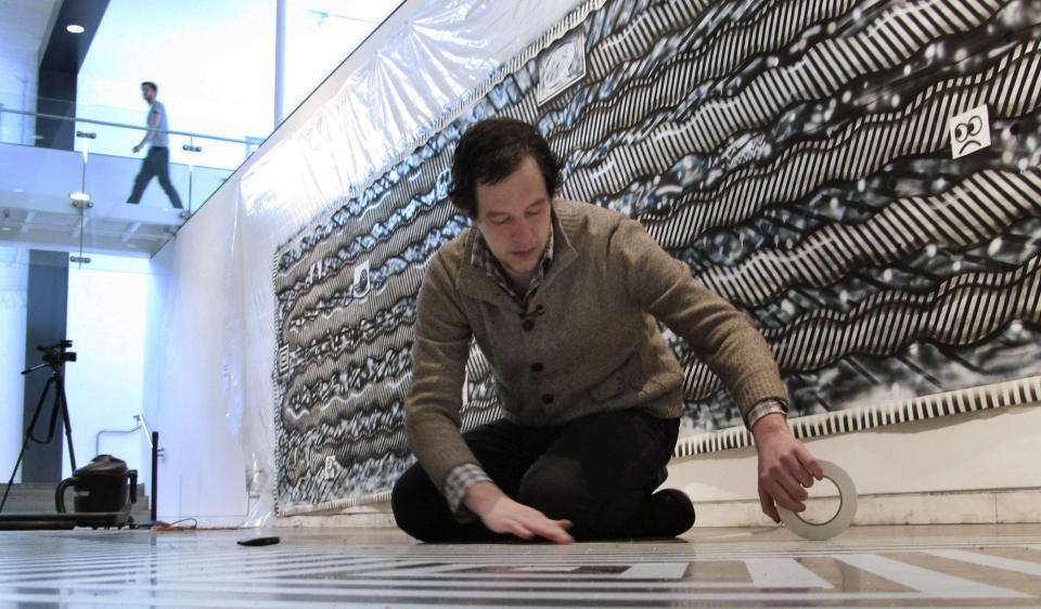 In this Tuesday, Feb. 19, 2013 photo, Ryan Travis Christian lays out a tape pattern on the floor in front of his wall-sized drawing at the Contemporary Art Museum in Raleigh, N.C. The Chicago artist completely reworked his wall-sized drawing several days into his first museum exhibition. (AP Photo/Allen Breed)