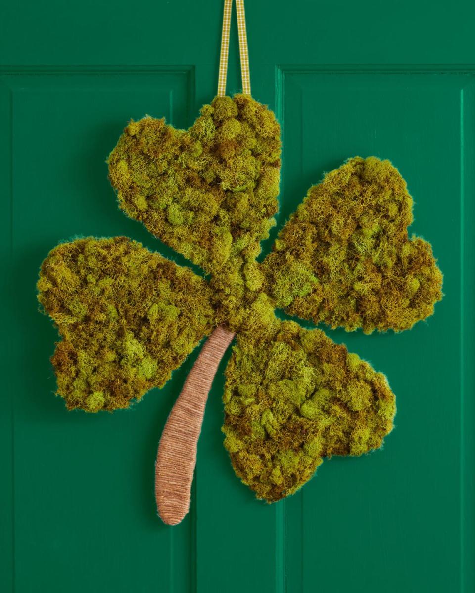 a four leaf clover wreath covered in moss with a rope stem hung on a dark green door