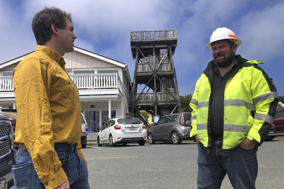 Mendocino County Supervisor Ted Williams, left, talks with Ryan Rhoades, superintendent of the Mendocino City Community Services District, which helps manage the water in the town's aquifer, in Mendocino, Calif., with an old water tower in the background on Wednesday, Aug. 4, 2021. Tourists flock to the picturesque coastal town of Mendocino for its Victorian homes and cliff trails, but visitors this summer will also find public portable toilets and dozens of signs on picket fences announcing the quaint Northern California hamlet: "Severe Drought Please conserve water." "This is a real emergency," said Rhoades, "We need assistance from the state, the county and the federal government." (AP Photo/Haven Daley)