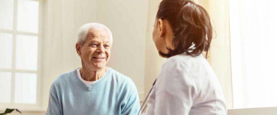 Man with white hair, smiling, talking to doctor in white coat