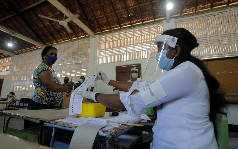 A Sri Lankan polling officer issues a ballot paper to a voter during a mock election ahead of the country's parliamentary poll in Negombo, Sri Lanka, Saturday, June 13, 2020. Sri Lanka's Election Commission set Aug. 5 as the new date for parliamentary elections after postponing them twice over the coronavirus pandemic. (AP Photo/Eranga Jayawardena)