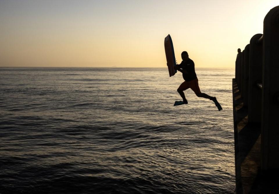 A surfer jumps off the pier in the early morning as the sun rises above North Beach Pier in Durban.