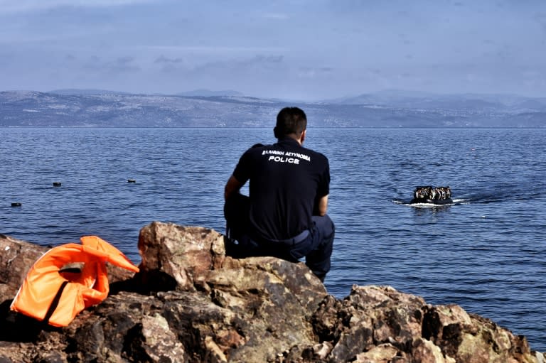 A policeman watches refugees and migrants arriving on the Greek island of Lesbos after crossing the Aegean sea from Turkey on October 5, 2015