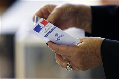 A woman holds an electoral card at a polling station in Paris March 23, 2014. REUTERS/Gonzalo Fuentes