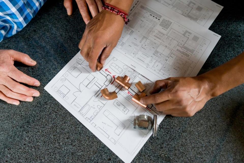 A person lays out small plumbing parts on top of a diagram of plumbing. 