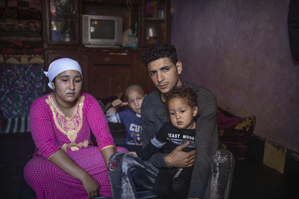 In this in Wednesday, March 25, 2020 photo, Younes and his wife, Ilham, pose for a photo with their children in their room in an overcrowded housing complex in Sale, near Rabat, Morocco. Hundreds of people live in crowded rooms in this Moroccan housing complex with no running water and no income left because of the coronavirus lockdown measures. However volunteers come to help clean as the government tries to protect the population from virus while not punishing the poor. (AP Photo/Mosa'ab Elshamy)