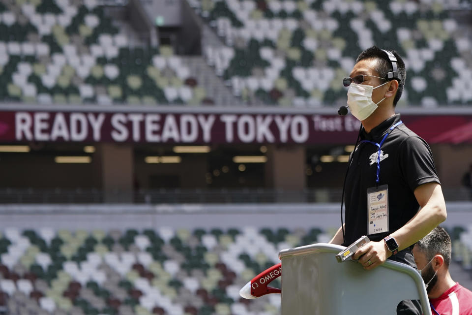 An official wears a face mask as he uses a starter pistol to signal the start a women's 100 meter heat at an athletics test event for the Tokyo 2020 Olympics Games at National Stadium in Tokyo, Sunday, May 9, 2021. Japan, seriously behind in coronavirus vaccination efforts, is scrambling to boost daily shots as the start of the Olympics in July closes in. (AP Photo/Shuji Kajiyama)