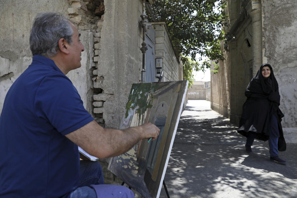 Painter Hassan Naderali greets a resident as he paints an old building in the historic neighborhood of Oudlajan, in Tehran, Iran, Monday, June 20, 2022. The overcrowded metropolis may be dusty and in need of beautification, but the old alleyways are nonetheless drawing throngs of artists out of their studios and into the streets. The practice thrived during the pandemic, as artists found solace and inspiration under the open sky when galleries and museums shuttered. (AP Photo/Vahid Salemi)