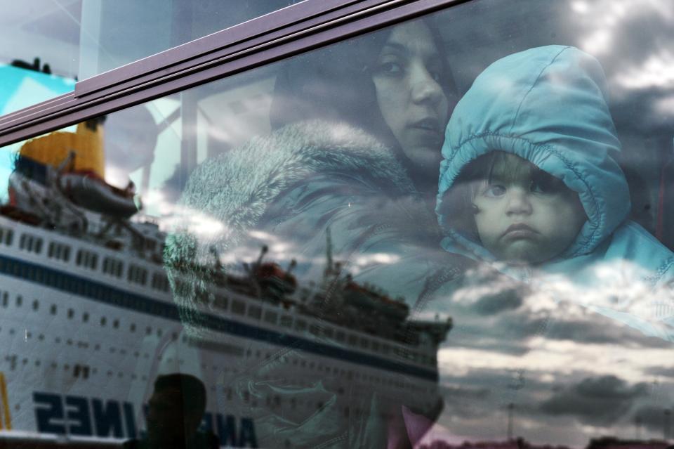 A woman and a child peer from a bus, after migrants and refugees disembarked from a government chartered ferry, seen in reflection, in the port of Piraeus in Athens on November 27, 2015.&nbsp;