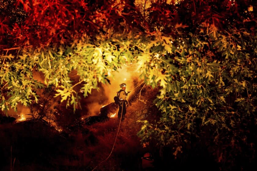 A firefighter sprays water on the Electra Fire burning in the Rich Gulch community of Calaveras County, Calif., on Monday, July 4, 2022. According to Amador County Sheriff Gary Redman, approximately 100 people sheltered at a Pacific Gas & Electric facility before being evacuated in the evening. (AP Photo/Noah Berger)