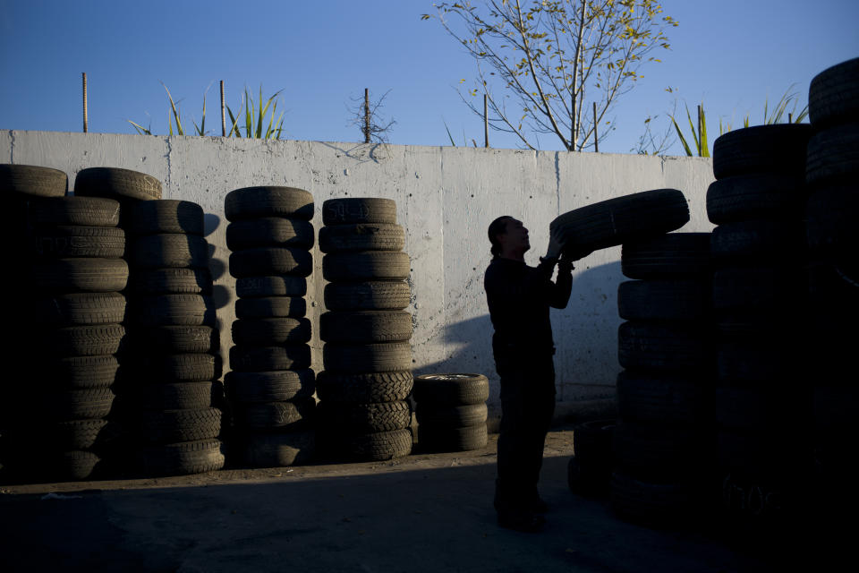 FILE- Junkyard employee Fabio Flores stacks up used tires at Aadlen Brothers Auto Wrecking, also known as U Pick Parts, in the Sun Valley section of Los Angeles on Nov. 19, 2015. The 13 largest U.S. tire manufacturers are facing a lawsuit from a pair of California commercial fishing organizations that could force the companies to either remove a chemical found in almost every tire that kills migrating salmon or obtain a permit to lawfully harvest species. (AP Photo/Jae C. Hong, File)